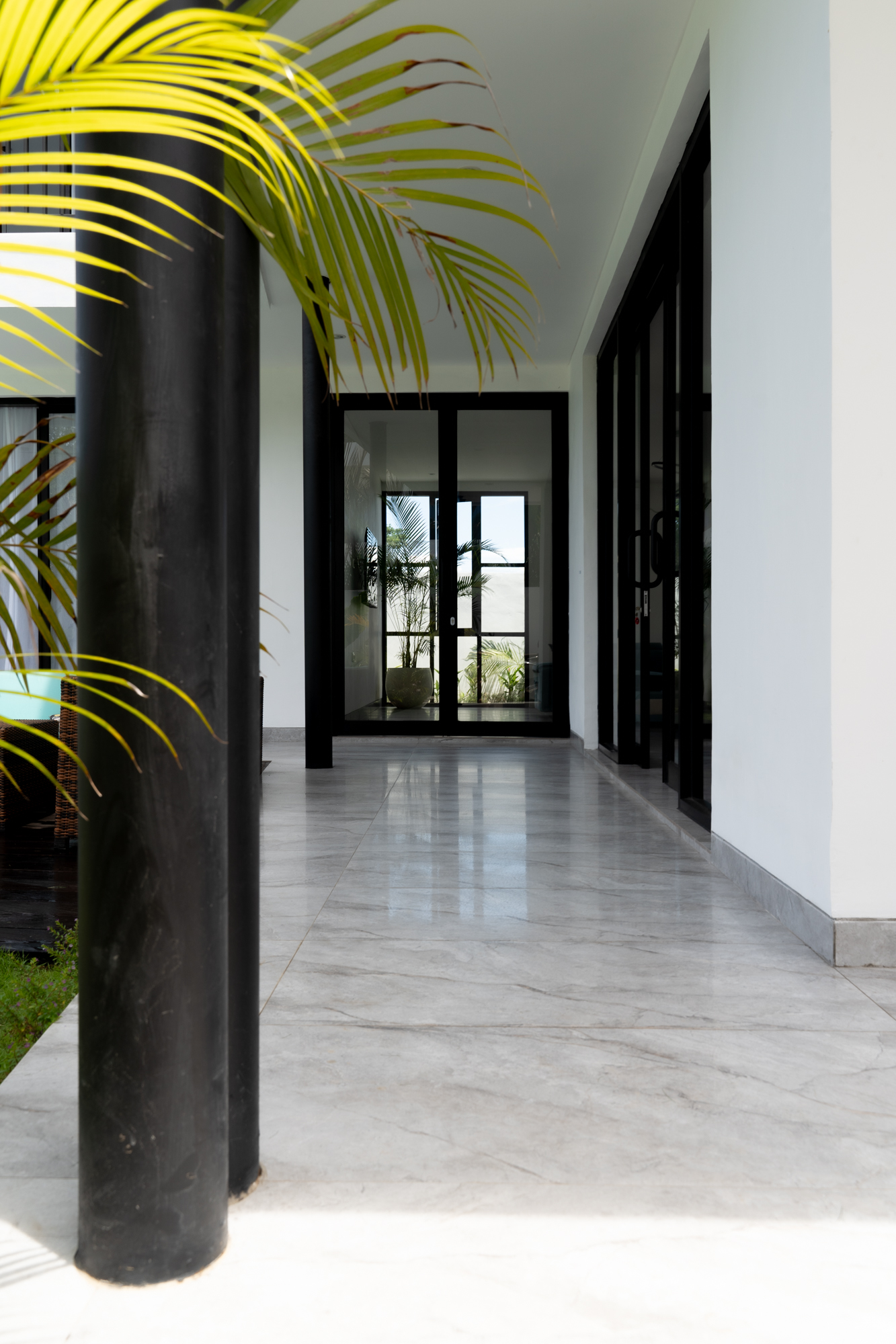 Modern entrance corridor of Villa Mila in Bali with marble floor, black-framed glass doors, tropical plants and minimalist architecture